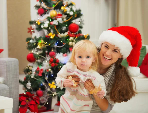 Retrato de la madre y comer bebé untado cerca del árbol de Navidad — Foto de Stock