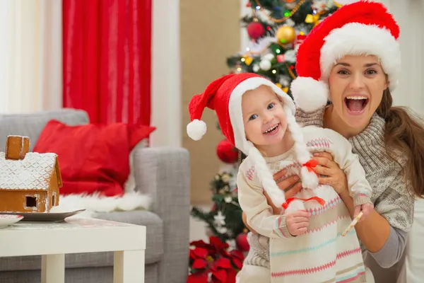 Portrait of mother and eat smeared baby in Christmas hats near C — Stock Photo, Image