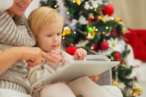 Madre mostrando al bebé algo en la tableta PC cerca del árbol de Navidad — Foto de Stock