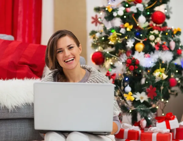 Leende ung kvinna med laptop sitter nära julgran — Stockfoto