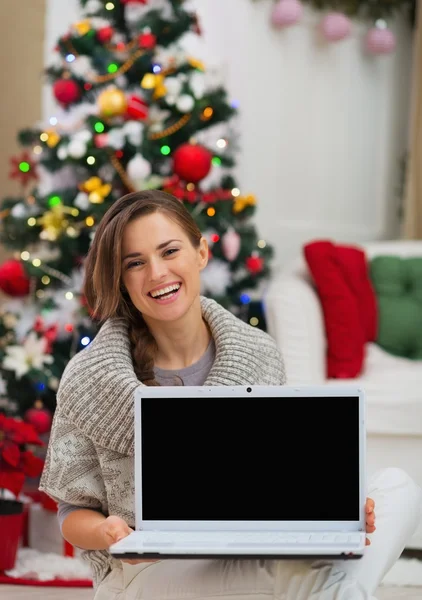 Mujer sonriente mostrando la pantalla en blanco del ordenador portátil cerca del árbol de Navidad —  Fotos de Stock