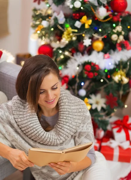 Glückliche junge Frau liest Buch in der Nähe von Weihnachtsbaum — Stockfoto