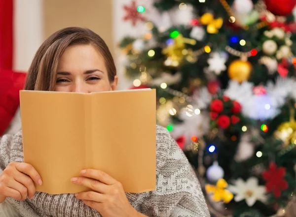 Mulher escondida atrás do livro na frente da árvore de Natal — Fotografia de Stock