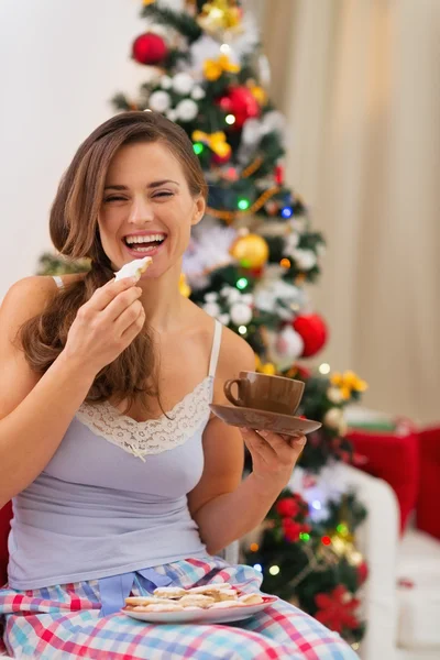 Happy young woman in pajamas eating cookies with hot chocolate n — Stock Photo, Image