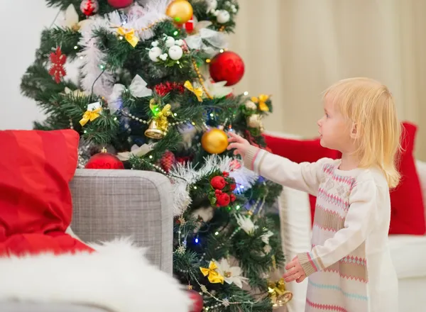 Baby berührt Weihnachtskugel am Weihnachtsbaum Stockbild