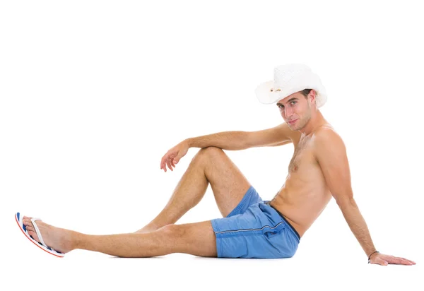 Smiling young man in shorts and hat sitting on floor — Stock Photo, Image