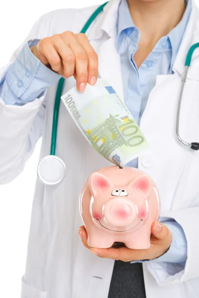 Closeup on medical doctor putting 100 euros note into piggy bank — Stock Photo, Image