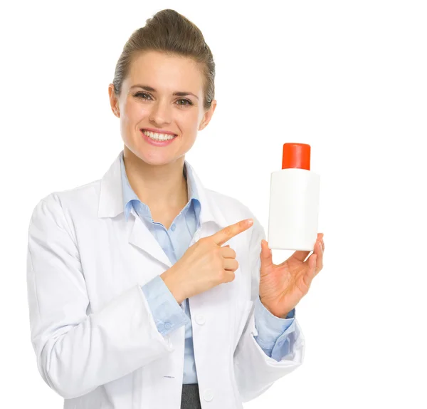 Улыбающийся косметолог указывает на бутылку солнцезащитного крема — стоковое фото