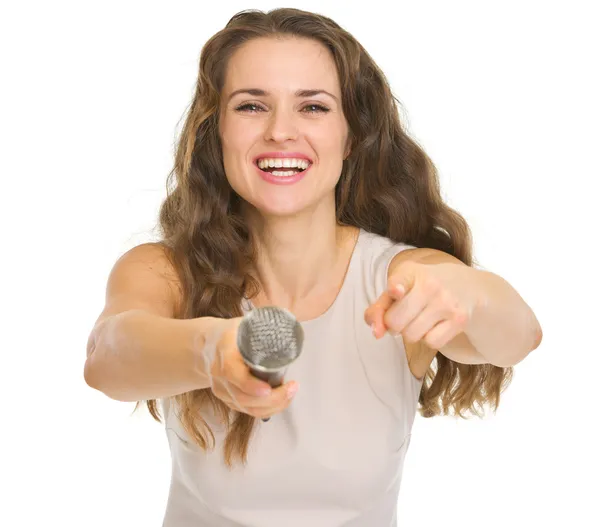 Young woman giving microphone and pointing in camera — Stock Photo, Image