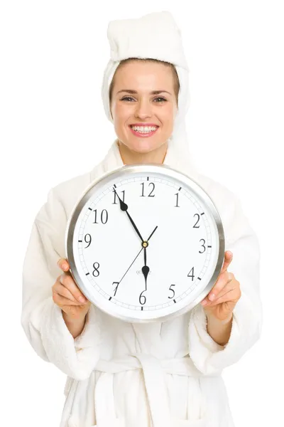Young woman in bathrobe showing clock and thumbs up — Stock Photo, Image