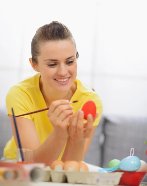 Счастливая молодая женщина рисует на пасхальном красном яйце — стоковое фото