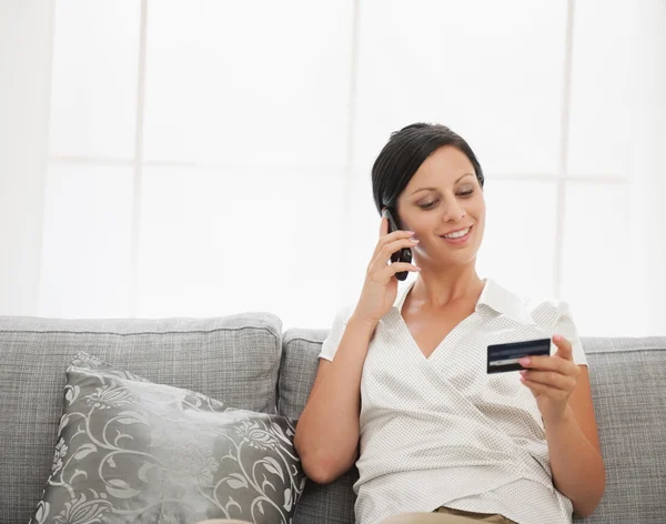 Boldog fiatal nő ül a kanapén, és beszél m hitelkártya — Stock Fotó