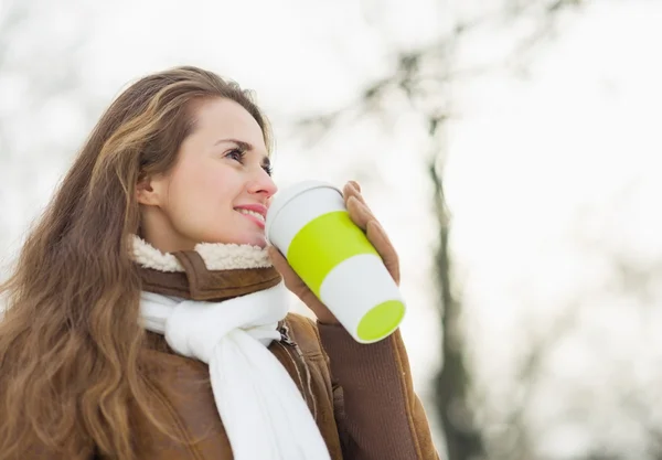 Happy young woman drinking hot beverage in winter park — Stock Photo, Image