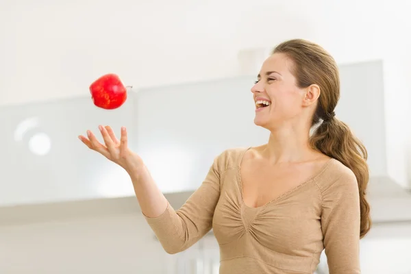 Mujer joven lanzando manzana en la cocina —  Fotos de Stock
