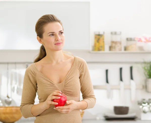 Portret van doordachte jonge vrouw met apple in moderne keuken — Stockfoto