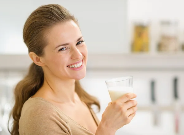 Portret van lachende jonge vrouw met glas melk in keuken — Stockfoto