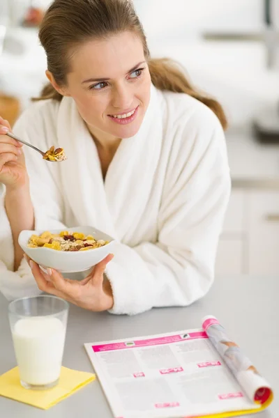 Thoughtful young woman in bathrobe eating breakfast in kitchen — Stock Photo, Image