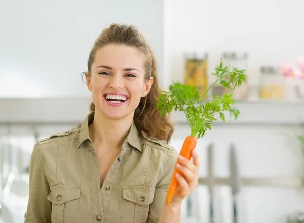 Sorridente giovane casalinga che tiene la carota in cucina — Foto Stock