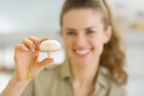 Smiling young housewife holding mushroom in kitchen — Stock Photo, Image