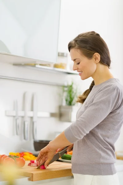 Jovem dona de casa feliz cortando legumes na salada na cozinha — Fotografia de Stock