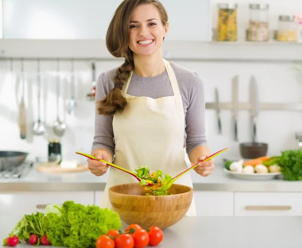 Glückliche junge Hausfrau mixt Gemüsesalat — Stockfoto