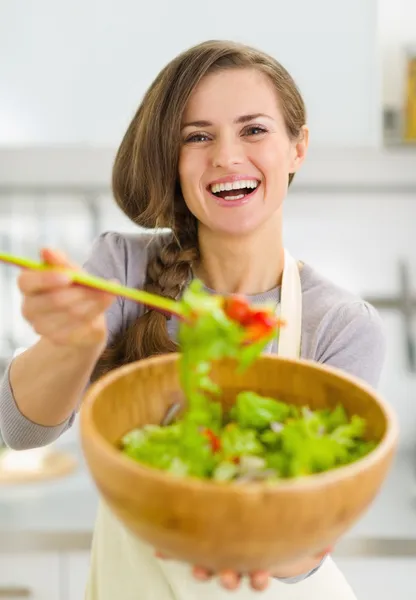 Jovem dona de casa feliz dando colher com salada de legumes — Fotografia de Stock