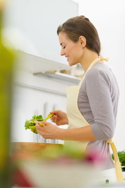 Jovem dona de casa feliz misturando salada na cozinha moderna — Fotografia de Stock