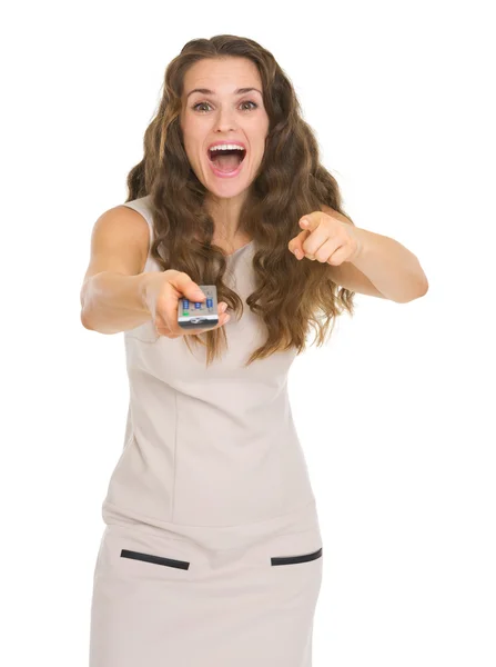 Surprised young woman with tv remote control pointing in camera — Stock Photo, Image