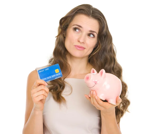 Jovem atenciosa segurando cartão de crédito e banco porquinho — Fotografia de Stock