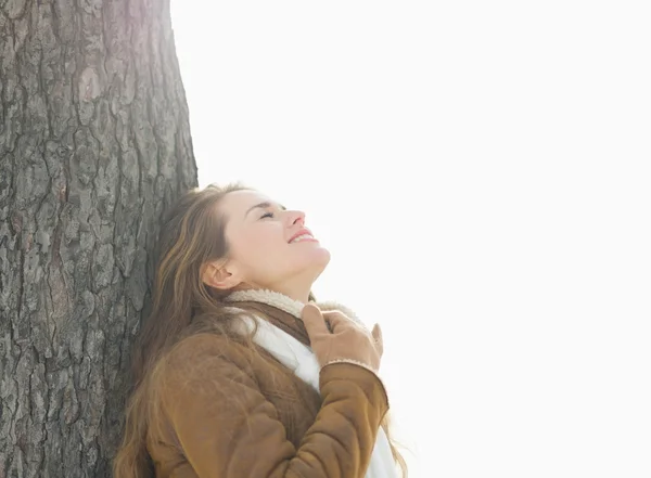 Happy young woman leaning against tree in winter park — Stock Photo, Image