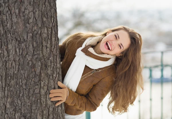 Felice giovane donna guardando fuori dall'albero — Foto Stock