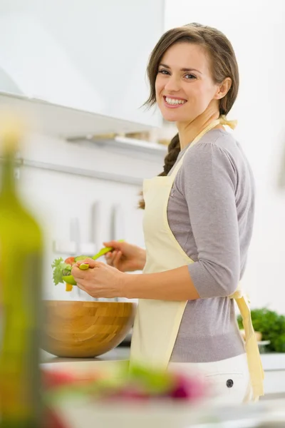 Lächelnde junge Hausfrau mixt Salat in moderner Küche lizenzfreie Stockbilder