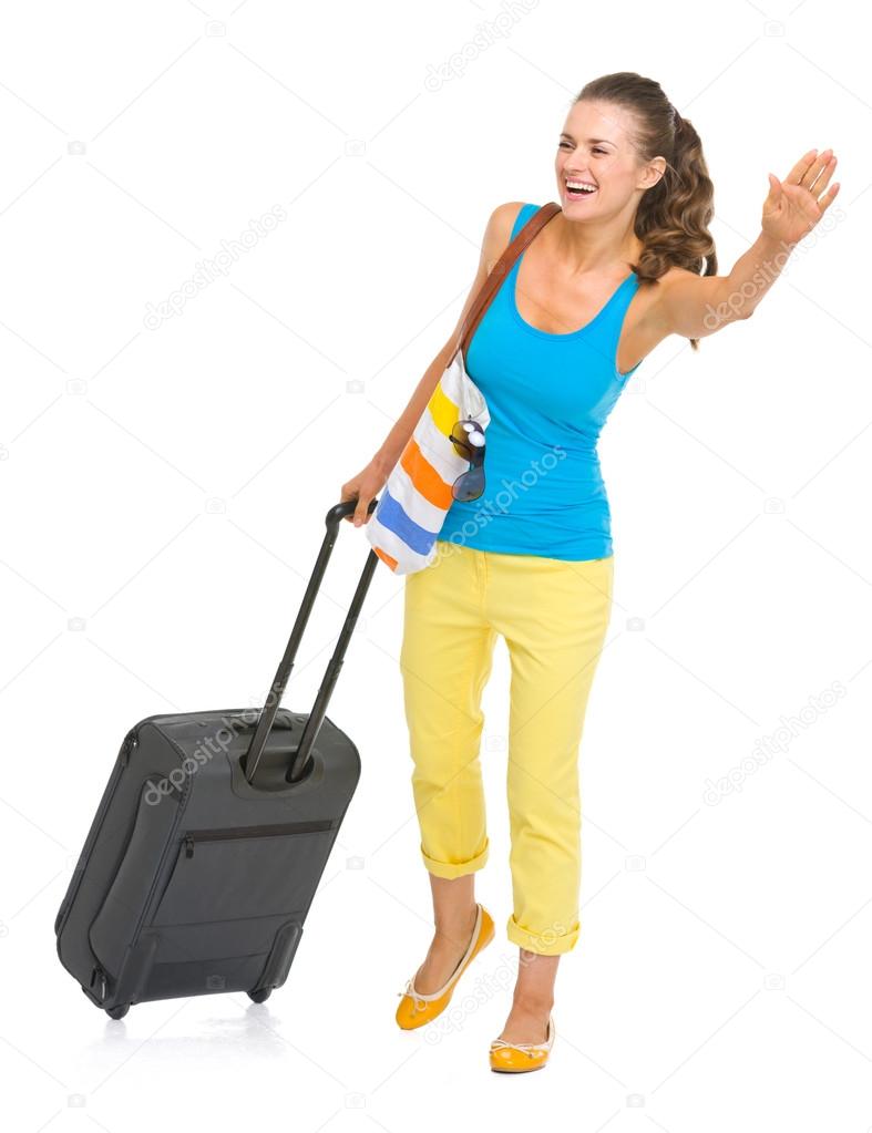 Smiling young tourist woman with wheel bag catching taxi