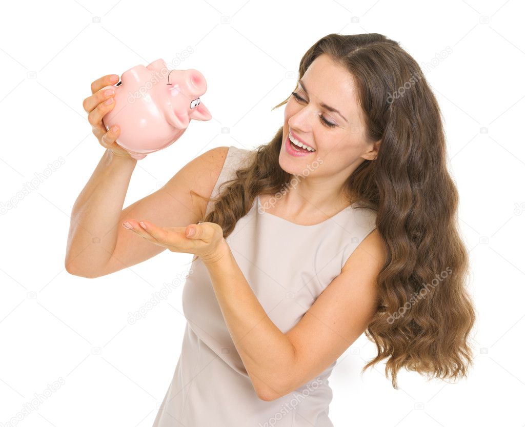 Happy young woman shaking out coins from piggy bank