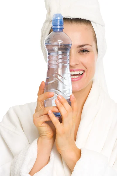 Lächelnde junge Frau im Bademantel versteckt sich hinter Flasche mit Wasser — Stockfoto