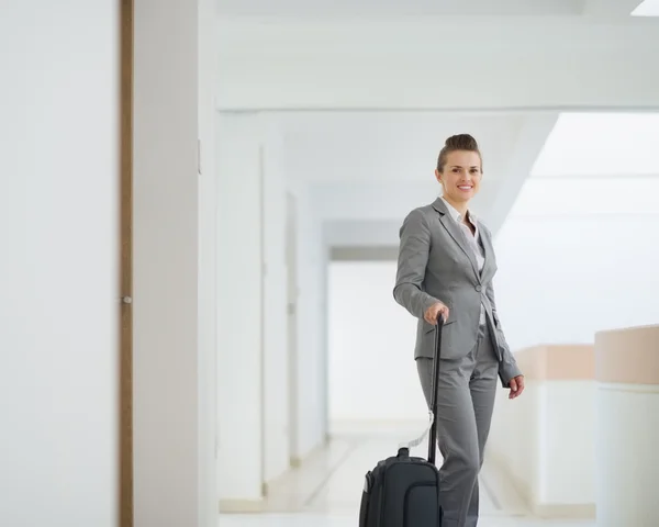 Smiling business woman with bag on wheels in business trip — Stock Photo, Image