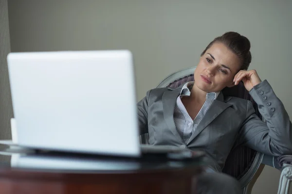 Tired business woman sitting in hotel room and looking on laptop — Stock Photo, Image