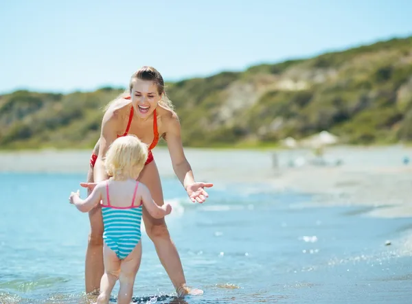 Mother and baby girl playing on sea coast — Stock Photo, Image