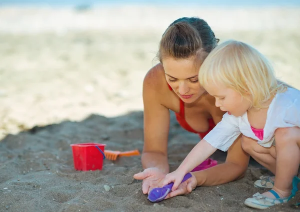 Happy mother and baby girl playing with sand on beach — Stock Photo, Image