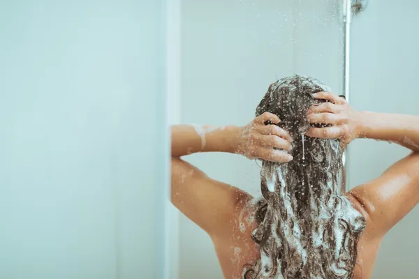 Mujer joven lavando la cabeza con champú. visión trasera — Foto de Stock