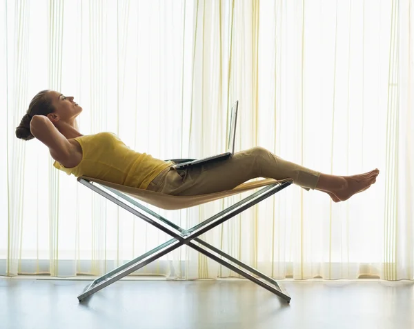 Silueta de mujer joven relajante en silla moderna con ordenador portátil —  Fotos de Stock