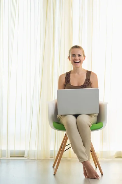 Happy young woman sitting on modern chair with laptop — Stock Photo, Image
