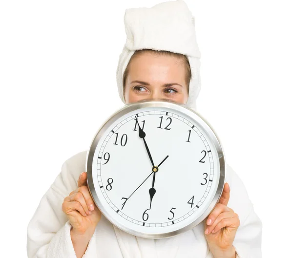 Young woman in bathrobe hiding behind clock Stock Photo