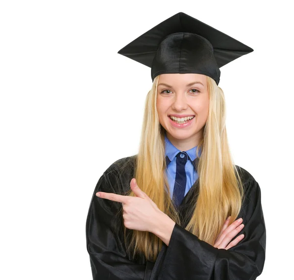 Smiling young woman in graduation gown pointing on copy space — Stock Photo, Image