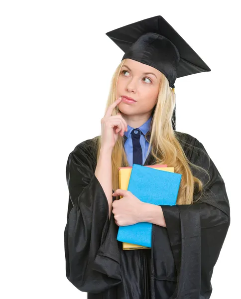 Doordachte jonge vrouw in afstuderen jurk met boeken — Stockfoto