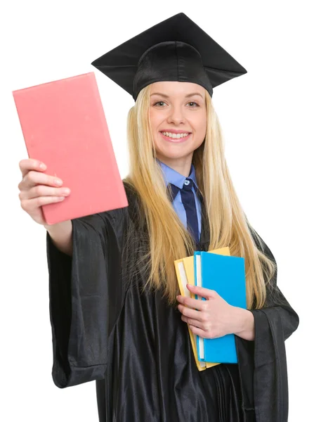 Lachende jonge vrouw in afstuderen jurk tonen boek — Stockfoto