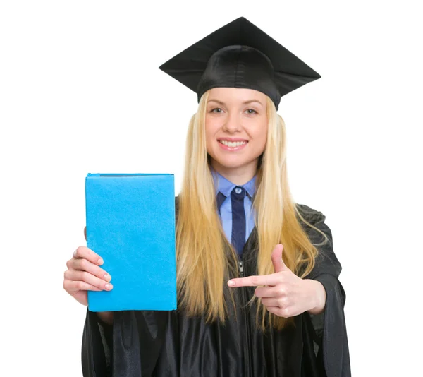 Young woman in graduation gown pointing book — Stock Photo, Image