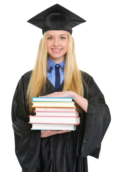 Sorrindo jovem mulher em vestido de graduação com pilha de livros — Fotografia de Stock