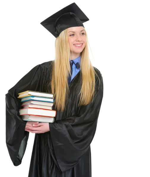 Mujer joven feliz en vestido de graduación con pila de libros que buscan —  Fotos de Stock