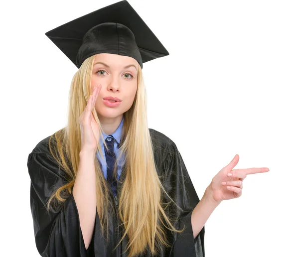 Jonge vrouw in afstuderen jurk wijzen op kopie ruimte — Stockfoto